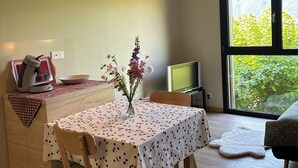 Un comedor con una mesa, sillas, un florero con flores, un hervidor y un televisor.