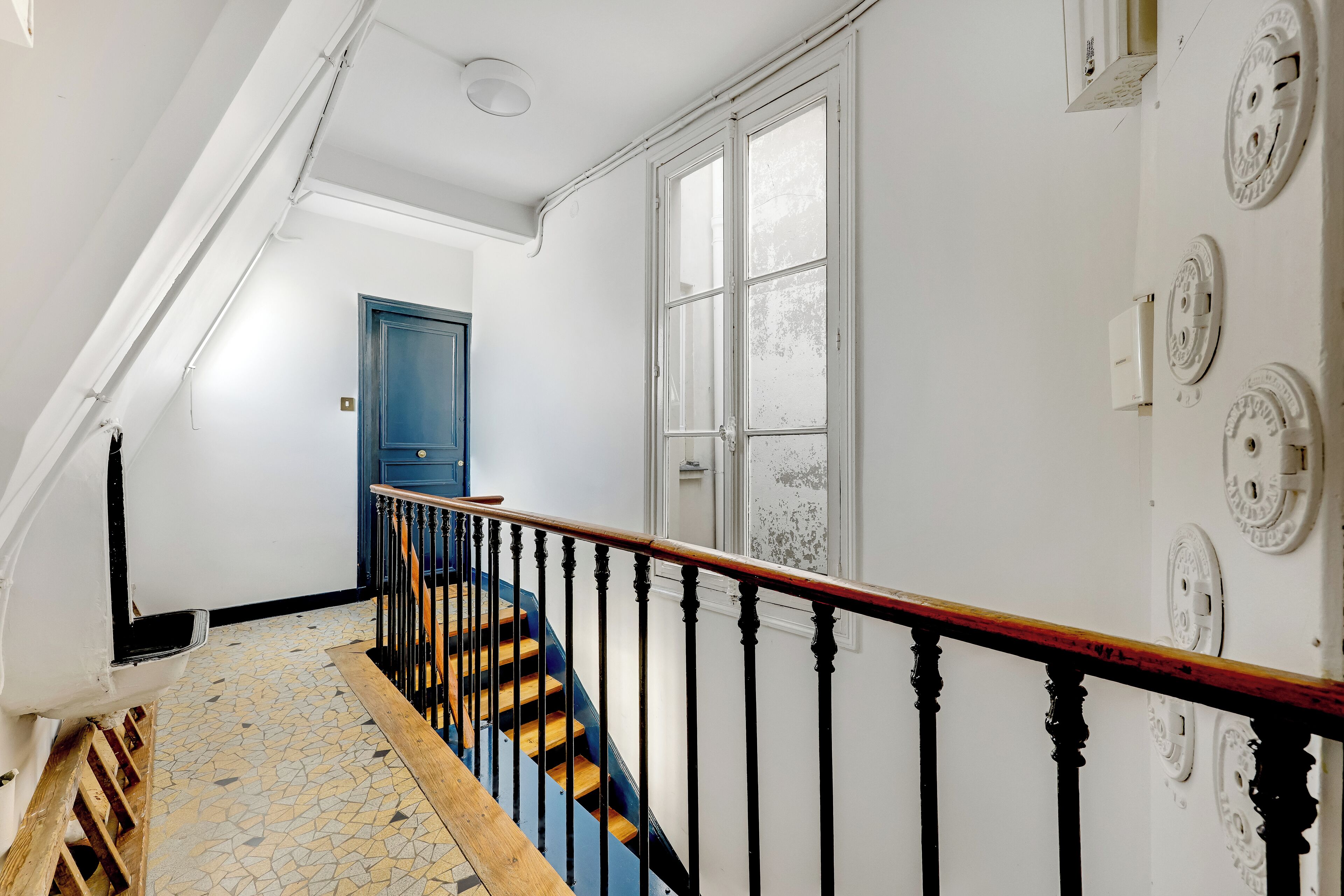 A staircase with a wooden handrail and black balusters, leading to a room with a blue door and a white wall with circular wall plates.