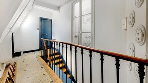 A staircase with a wooden handrail and black balusters, leading to a room with a blue door and a white wall with circular wall plates. - 26ROSIERS (Paris)