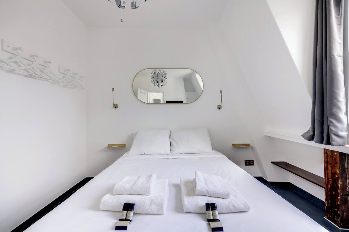 Une chambre d’hôtel moderne avec un grand lit, du linge de lit blanc, un miroir et une vue sur le ciel.