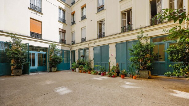 A courtyard with a central open space surrounded by buildings with green shutters and potted plants. - 26ROSIERS (Paris)
