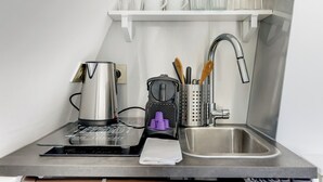 A kitchen with a coffee maker, a kettle, a toaster, a sink, and a shelf with cups and glasses. - 26ROSIERS (Paris)