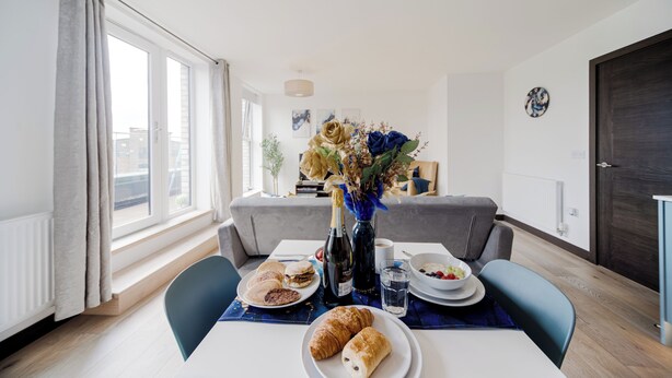 Ein Essbereich mit einem für das Frühstück gedeckten Tisch, darunter Croissants, eine Weinflasche und eine Vase mit Blumen.