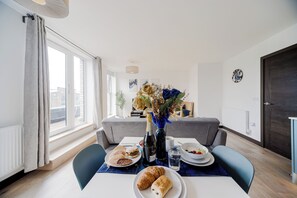 Uma sala de jantar com uma mesa posta para o café da manhã, incluindo croissants, uma garrafa de vinho e um vaso com flores.