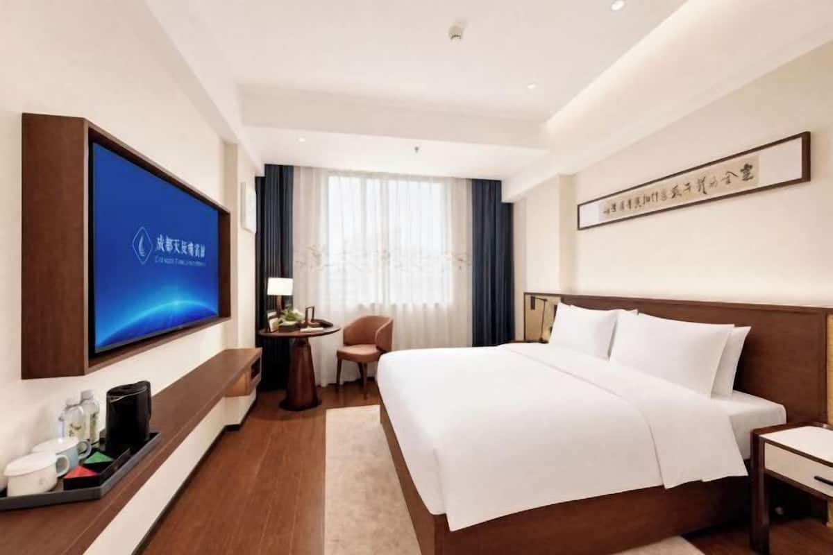 A hotel room with a large bed, a TV, a desk, and a chair.