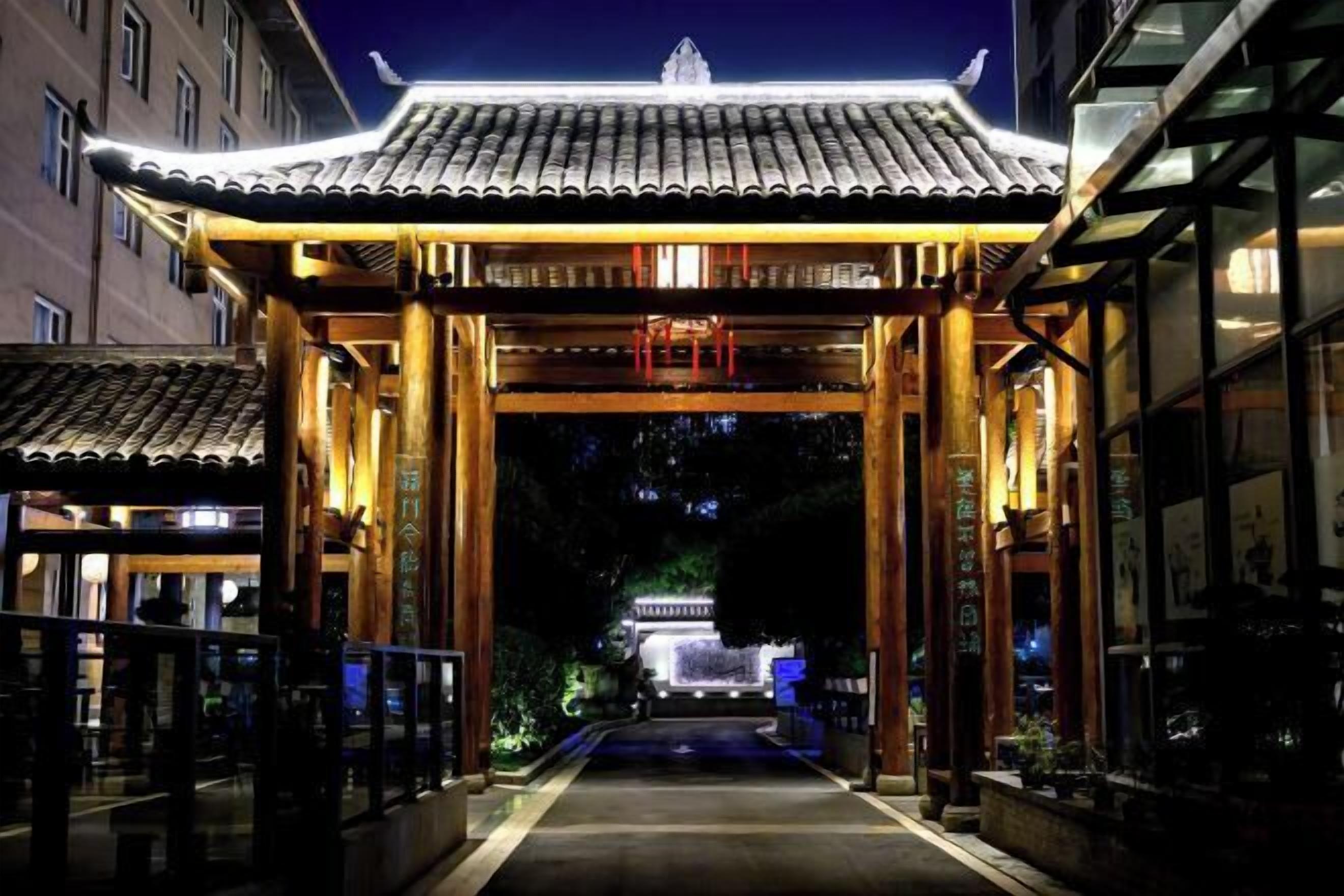 A traditional Japanese-style entrance with a tiled roof and wooden pillars, leading to a building with a visible garden in the background.