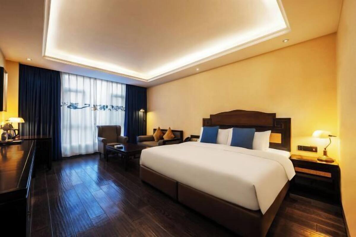 A hotel room with a large bed, a desk, a chair, and a nightstand with a lamp.