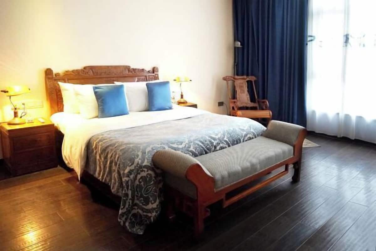A bedroom with a large bed, bedside tables, a bench, and a window with curtains.