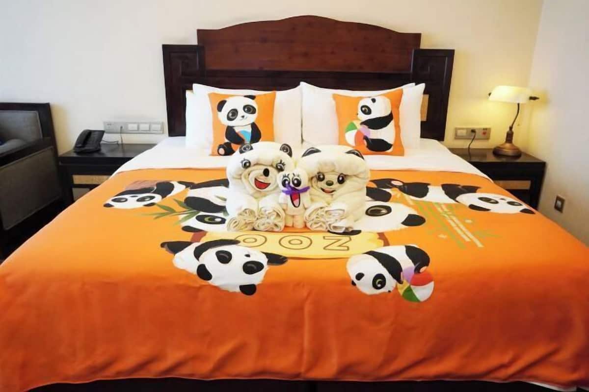 A bed with a panda-themed bedspread and pillows, a wooden headboard, a bedside table with a lamp, and a telephone.