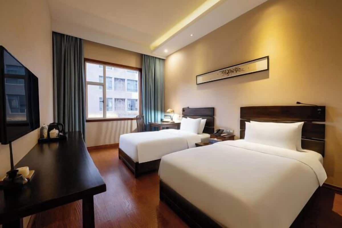 A hotel room with two beds, a desk, a TV, and a window with curtains.