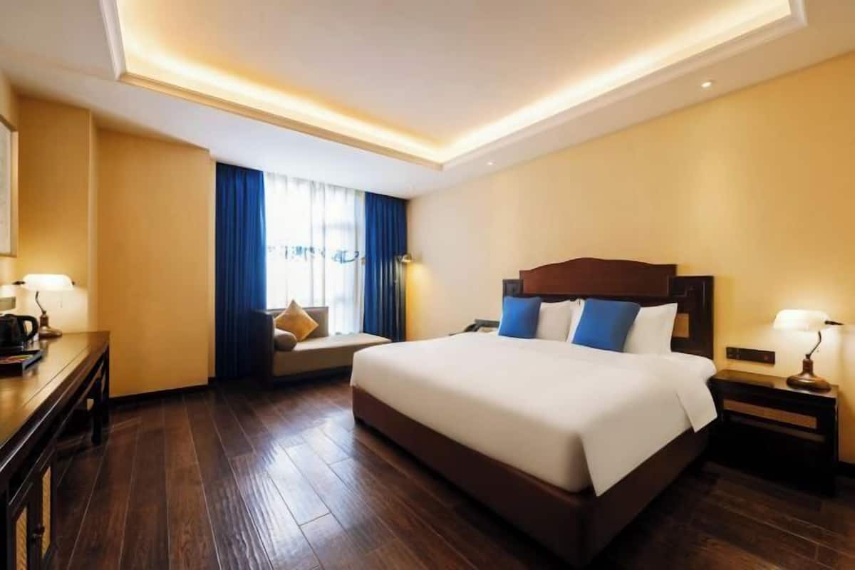A hotel room with a large bed, a desk, a chair, and a window with curtains.