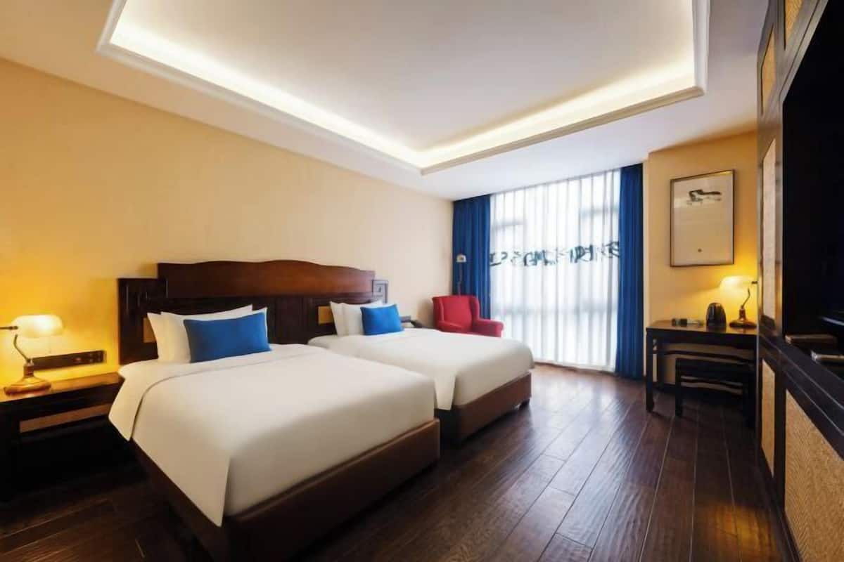 A hotel room with two beds, a desk, a chair, and a window with blinds.
