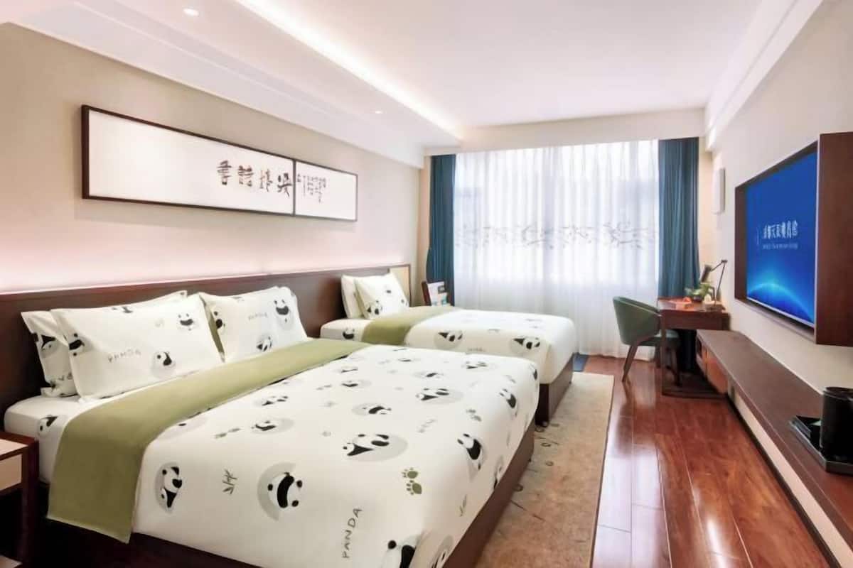A hotel room with two beds, a TV, a desk, and a window with curtains.