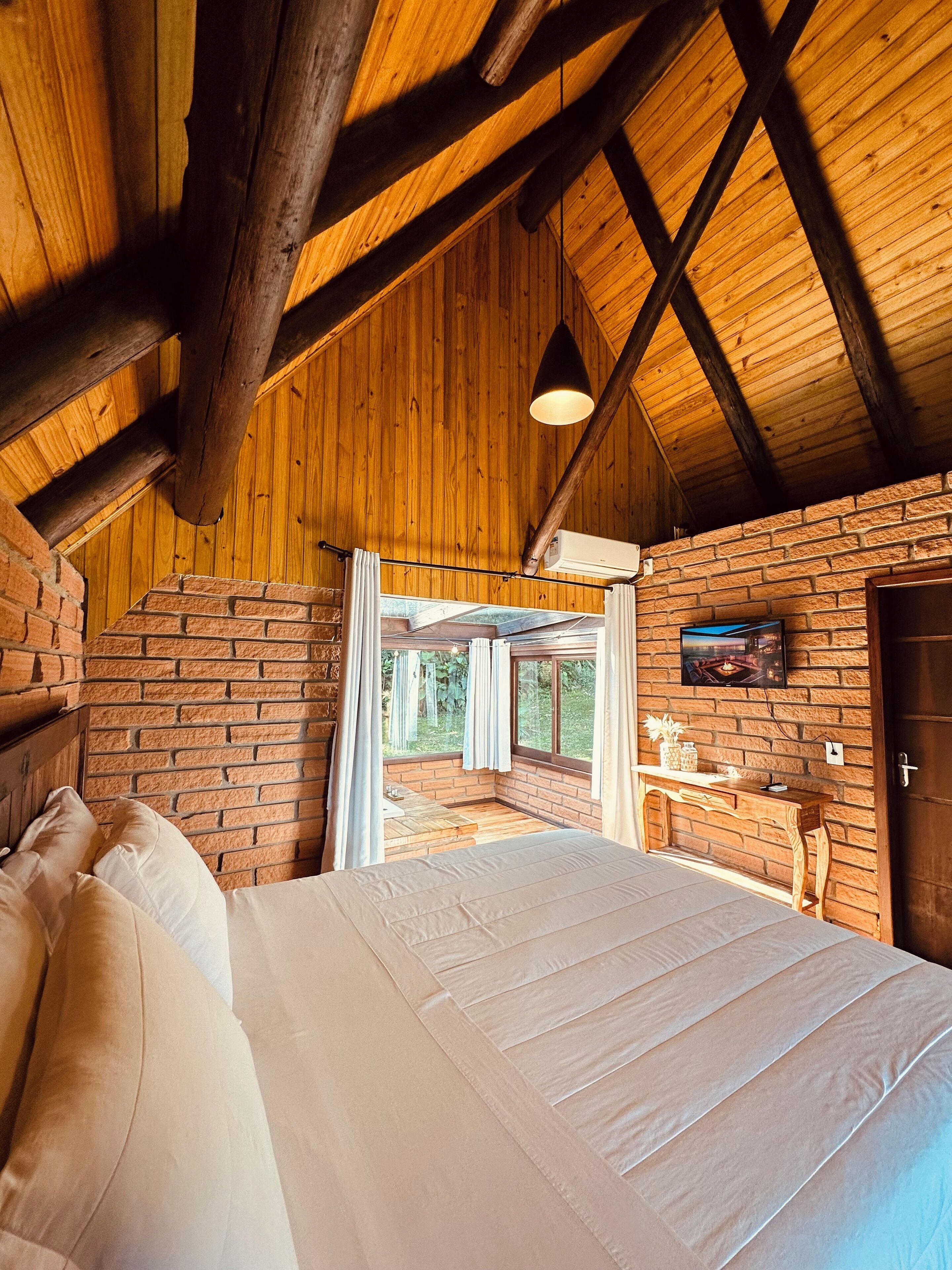 Un dormitorio con una cama grande, vigas de madera en el techo, una pared de ladrillo y una ventana con vistas a un jardín.
