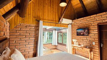 Un dormitorio con una cama grande, vigas de madera en el techo, una pared de ladrillo y una ventana con vistas a un jardín.