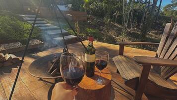A wooden deck with a fire pit, two glasses of red wine, and a bottle of wine.