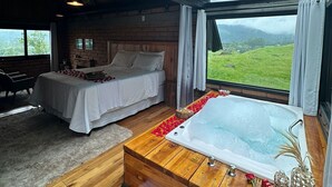 A bedroom with a large window, a wooden floor, a bed, a sofa, and a bathtub. - Maria Rita dos Canyons (Praia Grande)