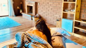A cozy room with a brick fireplace, a wooden bookshelf, and a television on the wall.