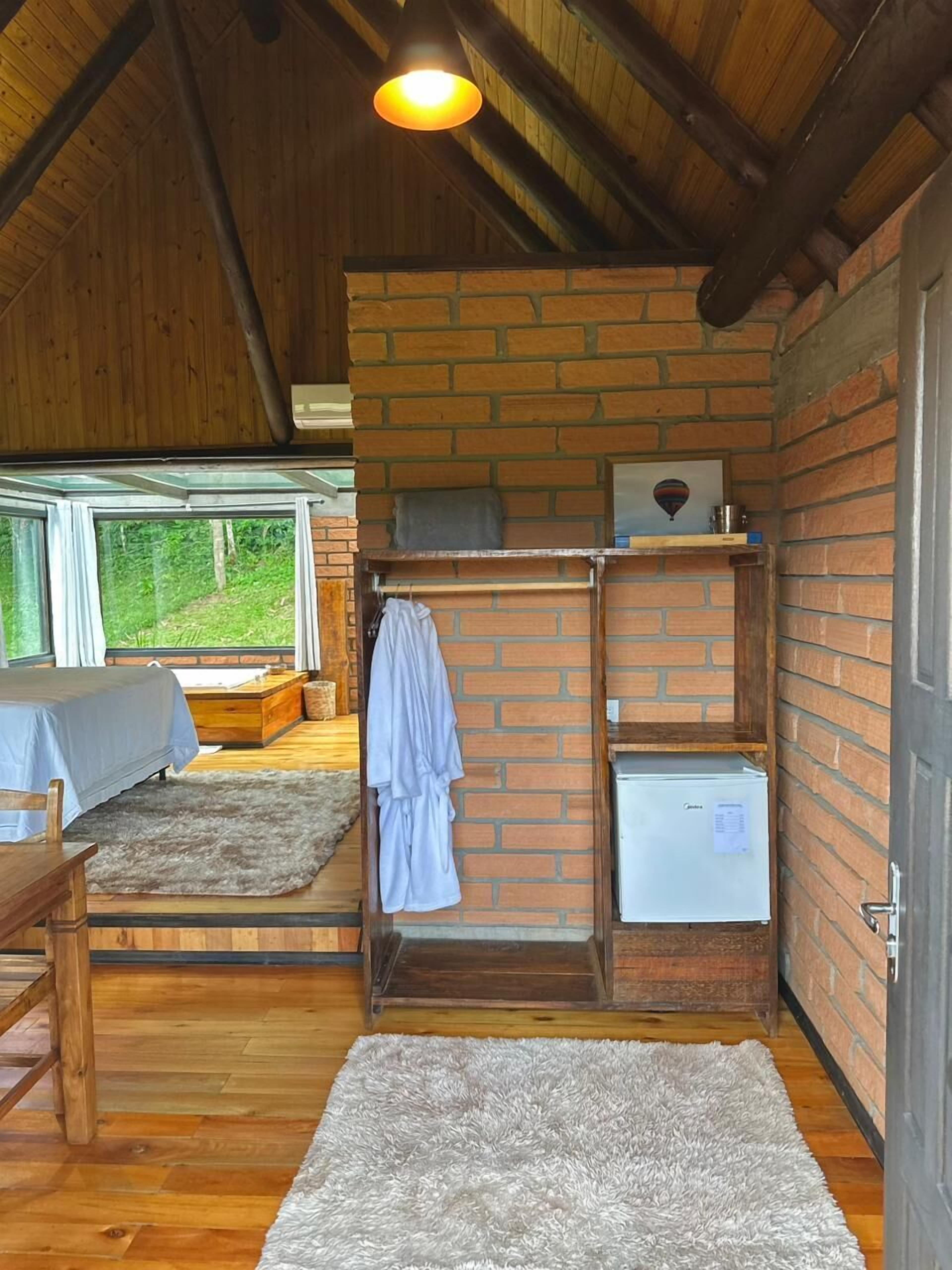 Ein gemütliches Zimmer mit Holzbalkendecke, einer Ziegelwand, einem Bett mit blauer Bettdecke, einem weißen, flauschigen Teppich und einem kleinen, weißen Kühlschrank.
