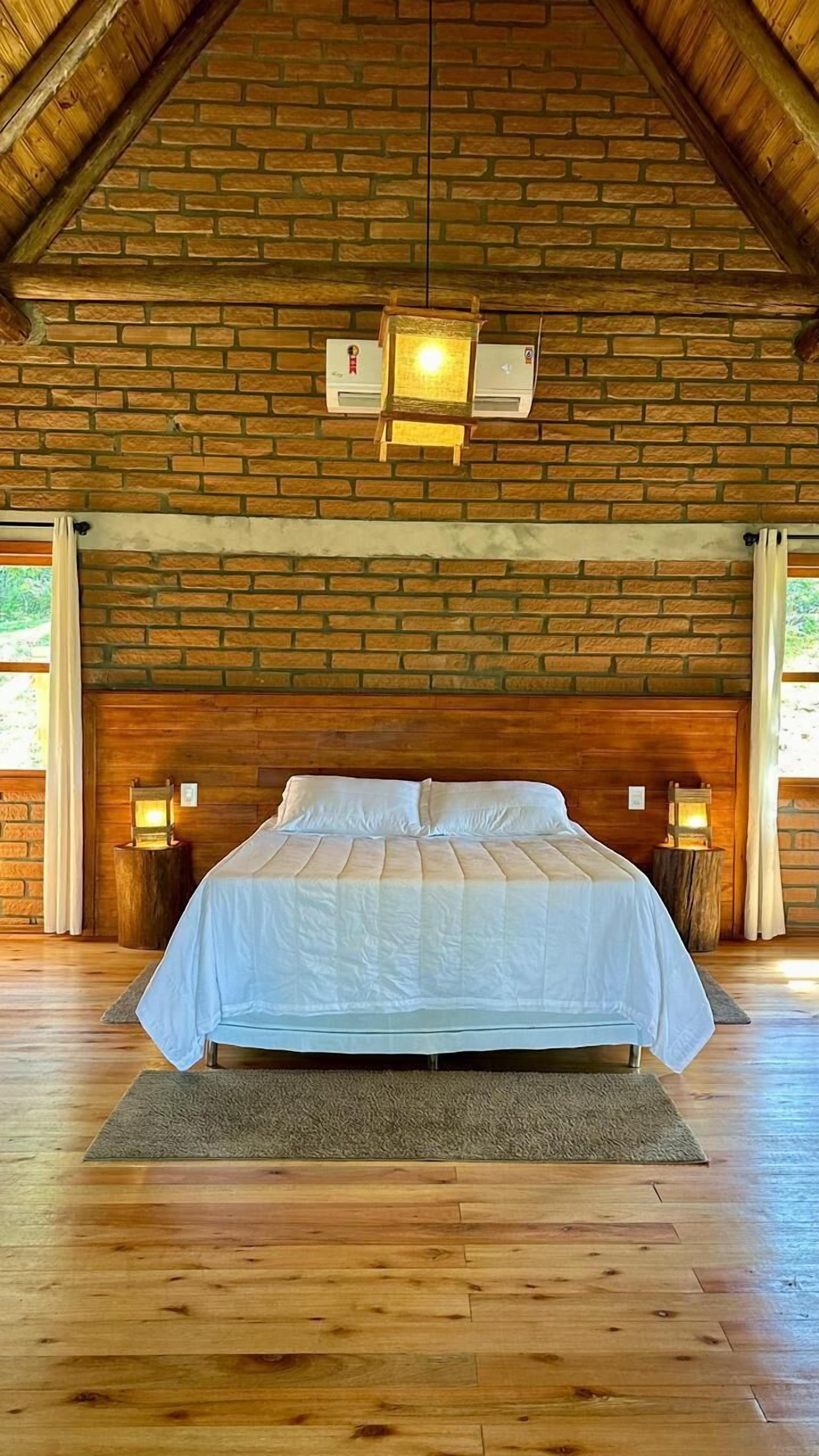 Una cama grande con cabecera de madera, dos lámparas de noche y una pared de ladrillo.