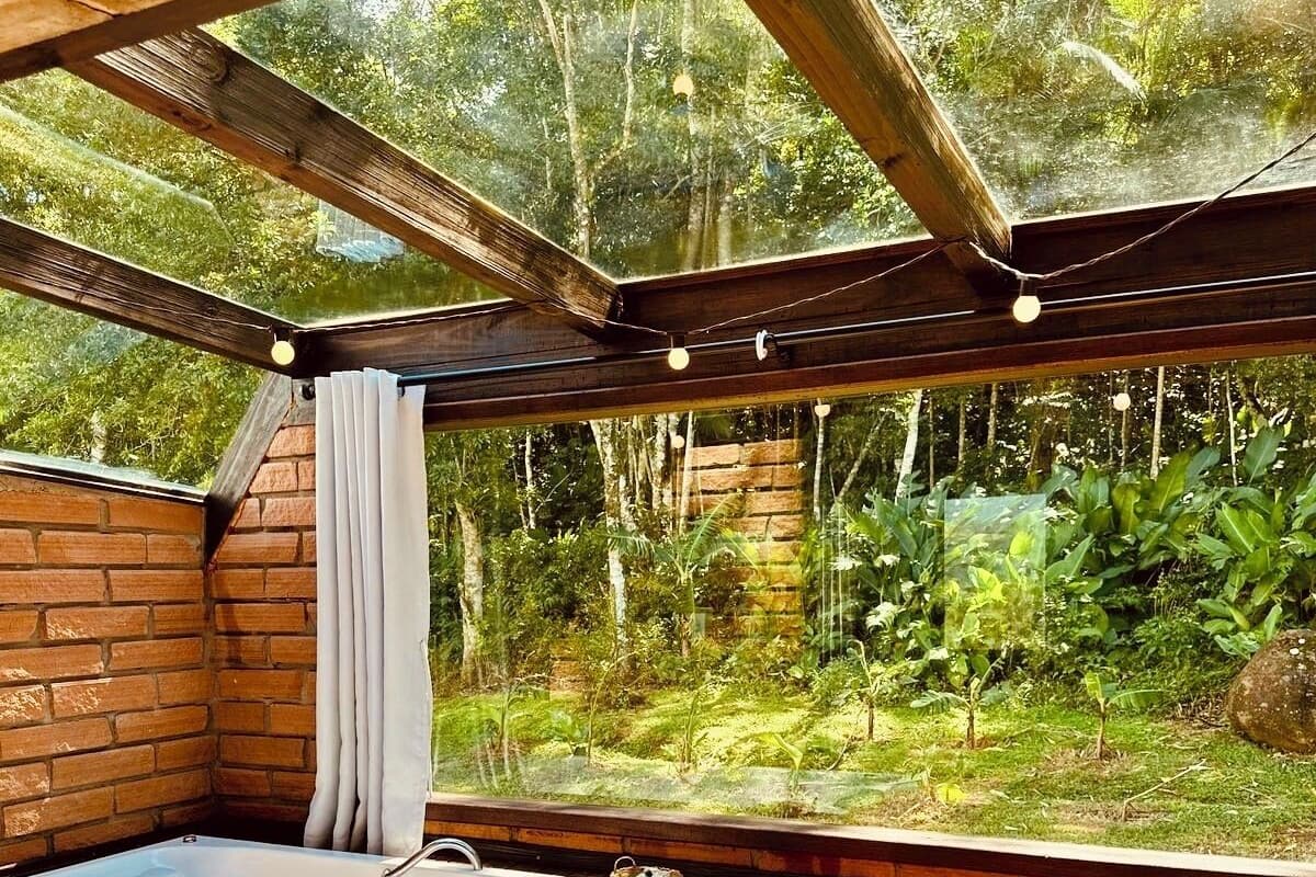 A hot tub in a wooden cabin with a glass ceiling, surrounded by lush greenery.
