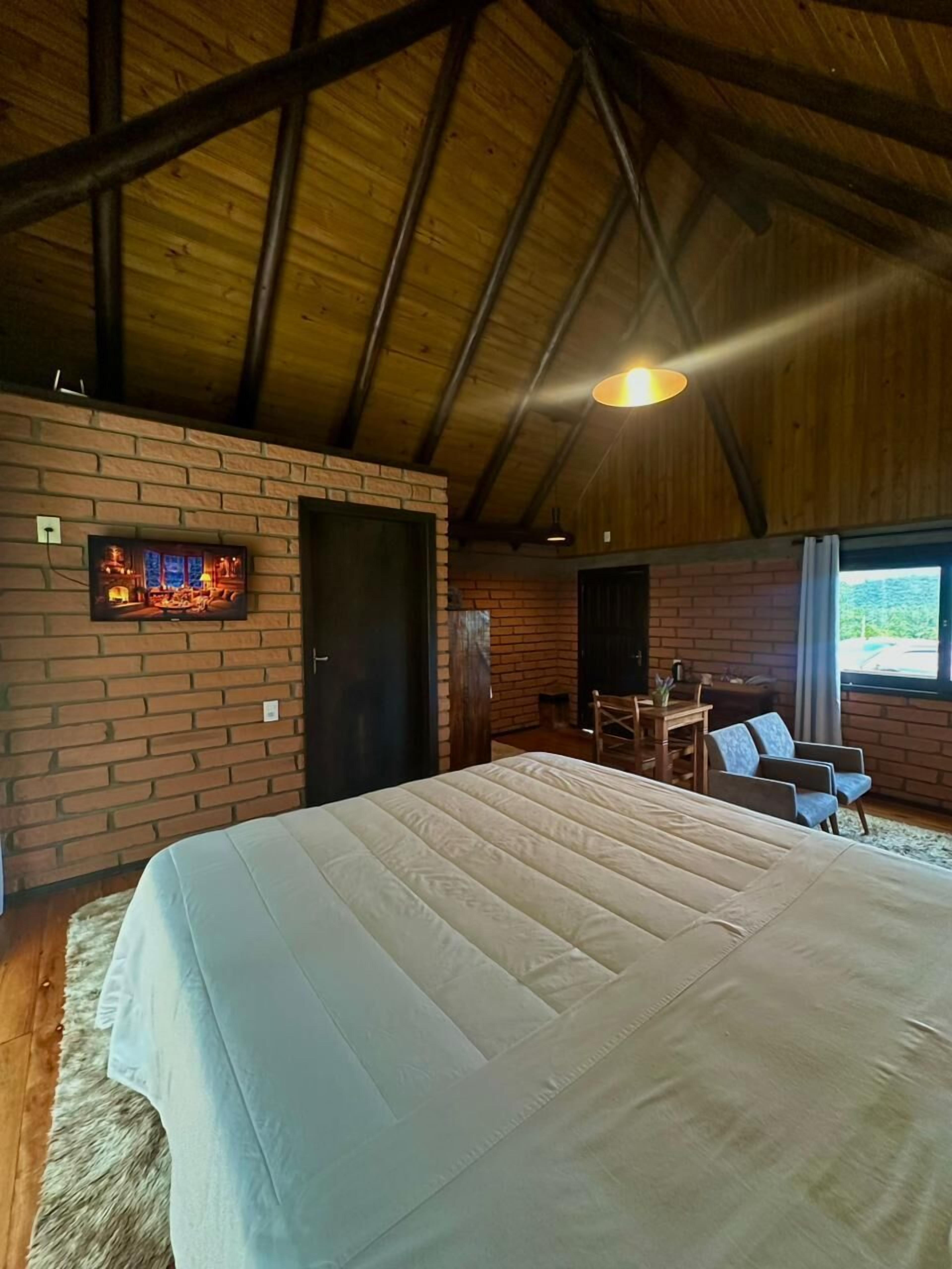 A spacious room with a large bed, a brick wall, and a wooden ceiling.