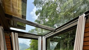 A wooden deck with a hot tub, large windows, and a view of greenery. - Maria Rita dos Canyons (Praia Grande)