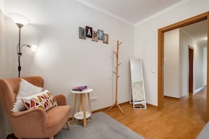 Quarto com poltrona rosa, uma pequena mesa branca com um livro, luminária de chão, cabideiro e um espelho apoiado na parede.