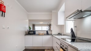 A modern kitchen with white cabinets, a granite countertop, a black induction cooktop, and a stainless steel range hood. - Sunflower Stay by Homie (Santa Cruz)