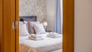 A neatly made bed with white linens and towels, a bedside lamp, and a floral wallpaper pattern. - Sunflower Stay by Homie (Santa Cruz)
