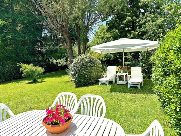 Eine Garten-Terrasse mit weißen Stühlen und einem Tisch, umgeben von üppigem Grün und Bäumen.