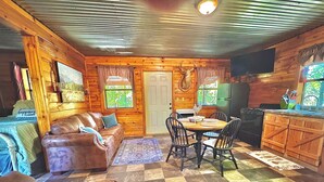 A cozy cabin interior with a brown leather couch, a dining table with chairs, a kitchen area, and a checkered floor. - Mossback Outfitters located in Wright City (Wright City)