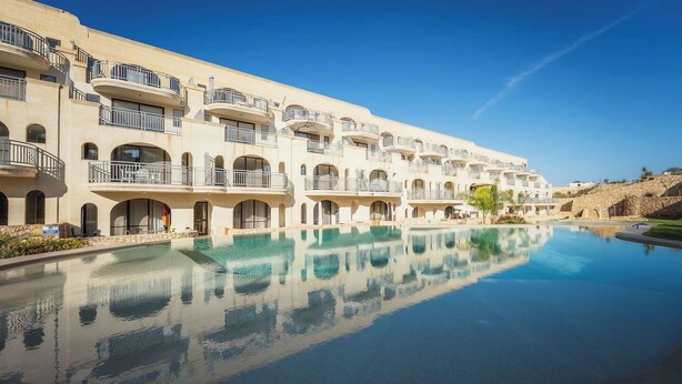 Un hotel con una piscina grande, varios balcones y un cielo azul despejado.