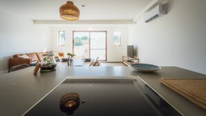 Una cocina moderna con una isla central, un comedor con sofá y un amplio ventanal que proporciona luz natural.