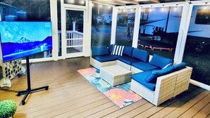 A cozy outdoor living area with a TV, wicker furniture, and a view of a street.