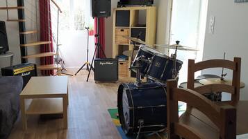 A room with a drum set, a Marshall amplifier, a bookshelf, and a window with curtains.