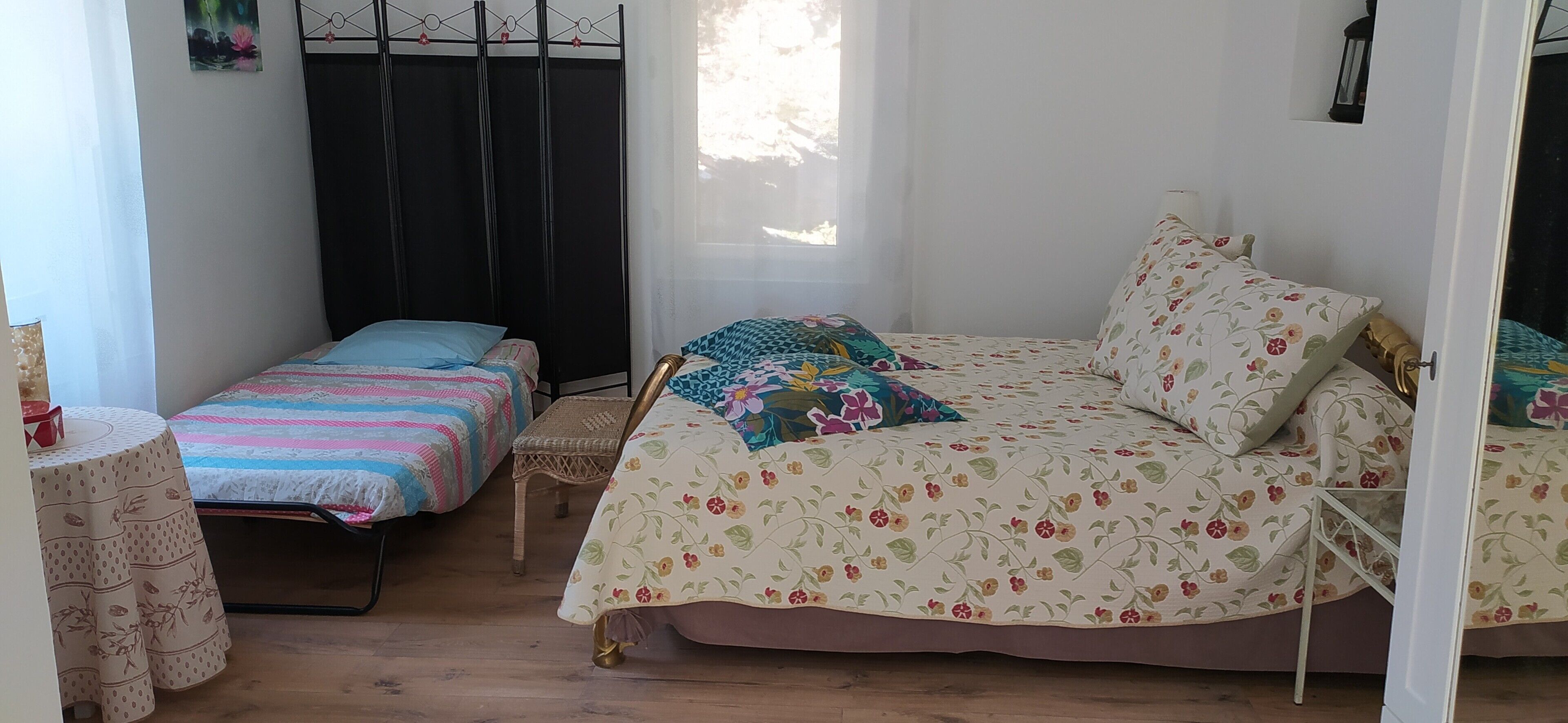 A bedroom with two beds, a window, a chair, and a small table.