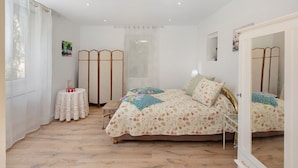 Un dormitorio con cama, una mesita redonda, un espejo y una ventana con cortinas.