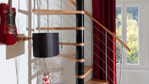 Una escalera de caracol con escalones de madera y barandilla negra, una guitarra roja y una ventana con vistas a árboles.