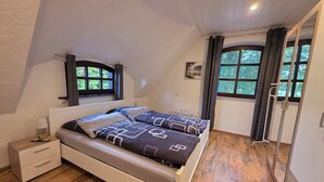 A bedroom with a bed, a nightstand, a dresser, and two windows with curtains. - Vacation apartment "Hahnskamp" / 2-6 pers. - Vacation on the farm - (Hamminkeln)