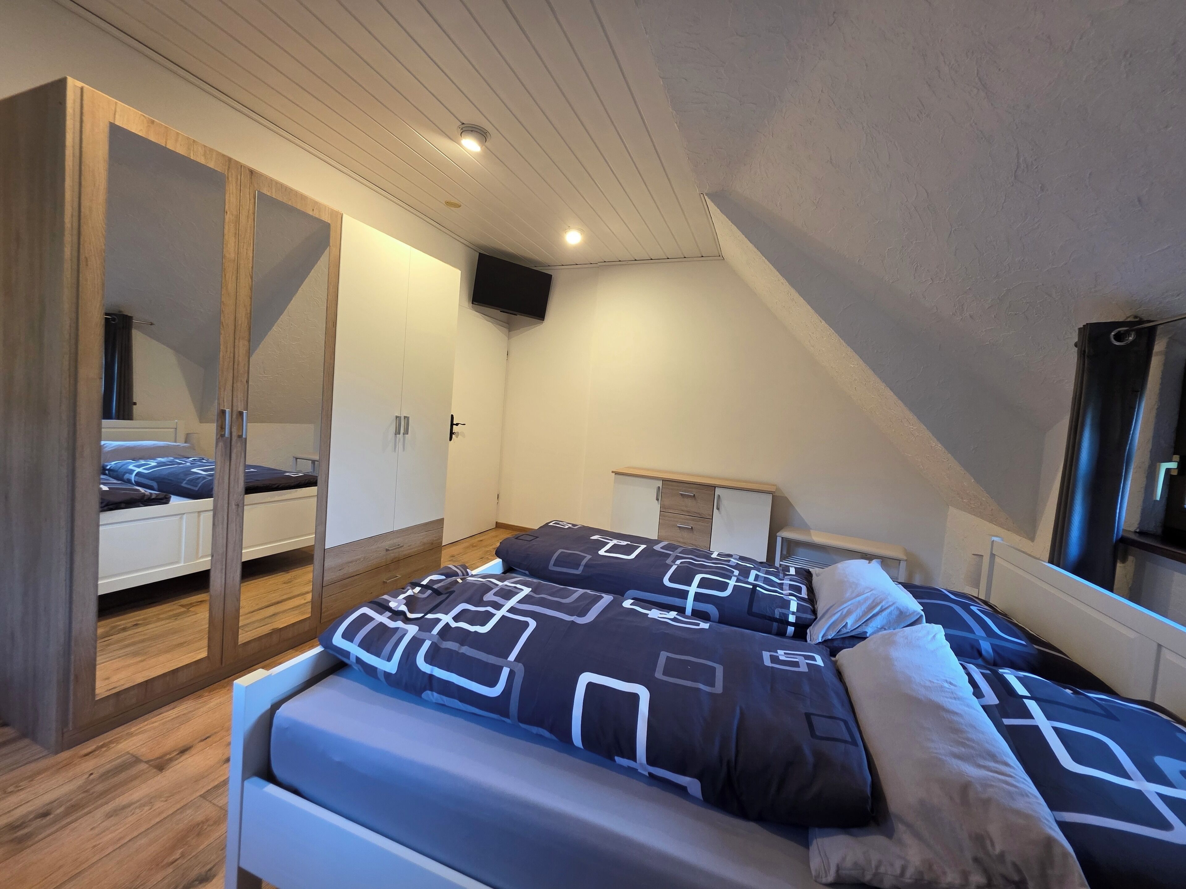 A bedroom with a loft bed, wooden wardrobe, and a TV mounted on the wall.