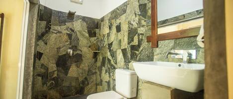 A bathroom with a toilet, sink, and a shower area with stone walls.