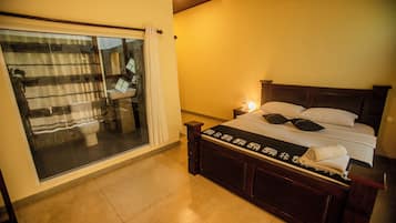 Un dormitorio con un amplio ventanal corredera que da a un balcón, una cama de madera con ropa de cama blanca y una mesita de noche con lámpara.