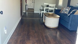 Una sala de estar moderna con piso de madera oscura, un sofá azul y un comedor con sillas blancas.