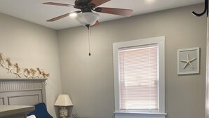 Un dormitorio con cama, ventilador de techo, ventana con persianas y decoración de estrella de mar en la pared.