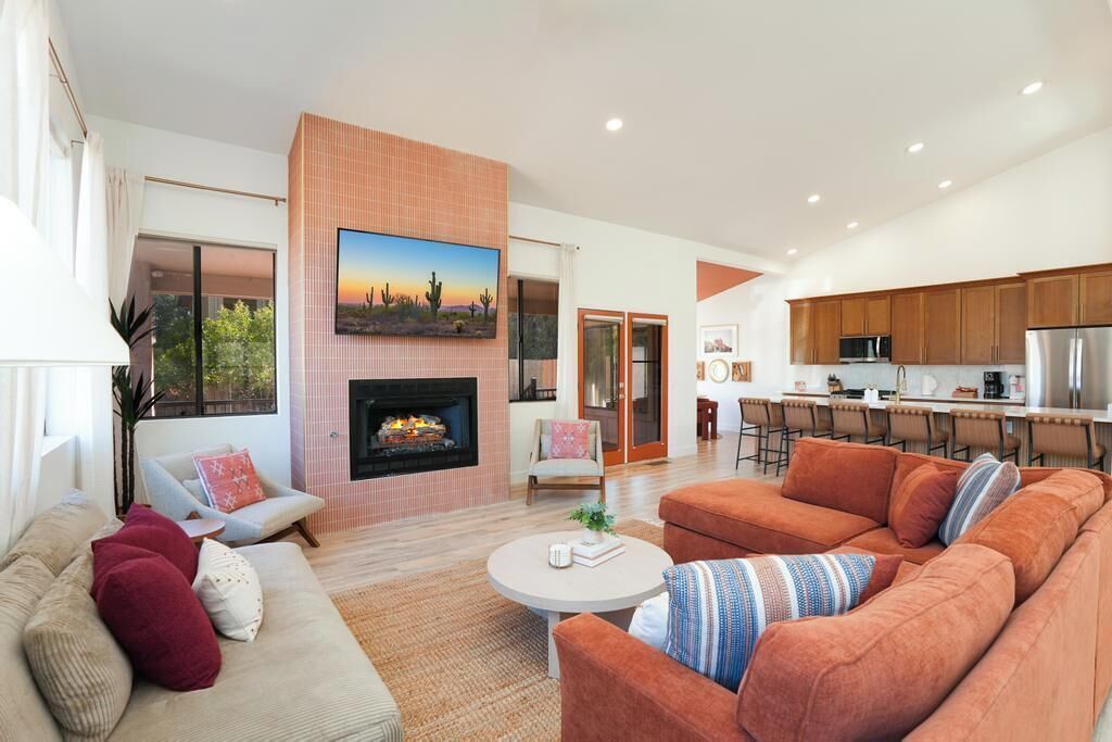 Una sala de estar moderna con chimenea, televisor grande y área de cocina con armarios de madera y barra.