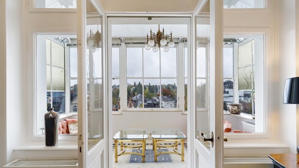 Um quarto com uma janela grande, um candelabro, uma mesa e um radiador.