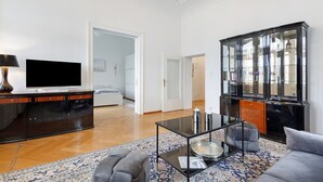 Uma sala de estar moderna com televisão de tela plana, mesa de centro de vidro, sofá, armário com portas de vidro e um candelabro.