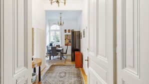 Um corredor com portas brancas, um candelabro, uma área de jantar com mesa e cadeiras, e um tapete.