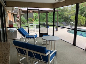 Ein Wintergarten mit Blick auf einen Swimmingpool, Gartenmöbel und einer überdachten Terrasse.